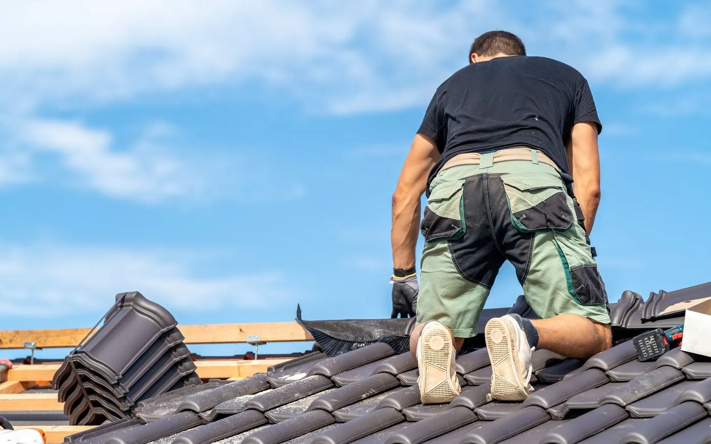 Roofer working on a tiled roof under a blue sky