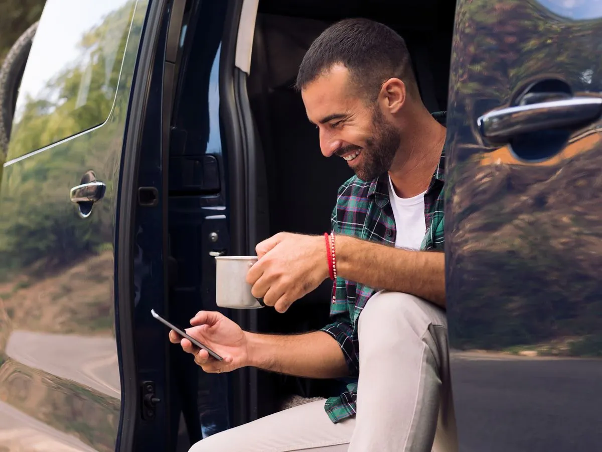 Tradesman checking his phone from the door of his van