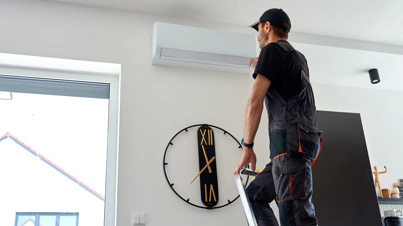 Engineer on a stepladder checking a wall-mounted indoor air conditioning unit in a living room