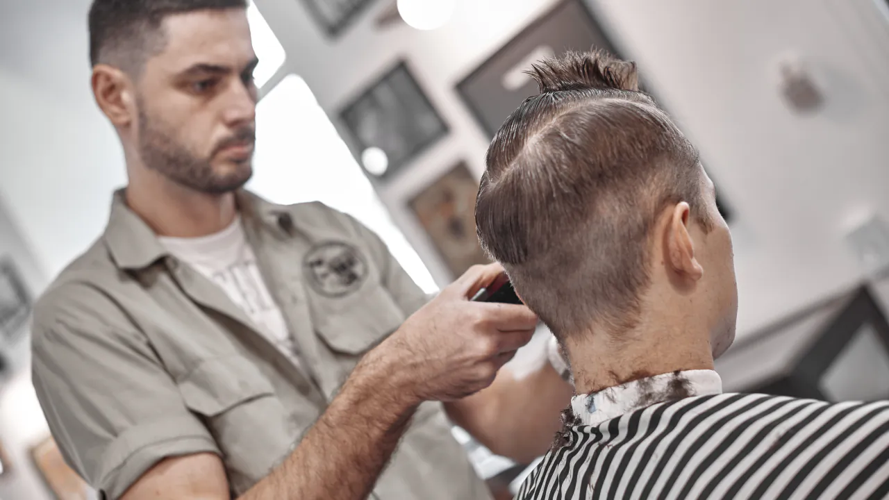Barber shaping a client's fade with clippers and a comb in a barbershop