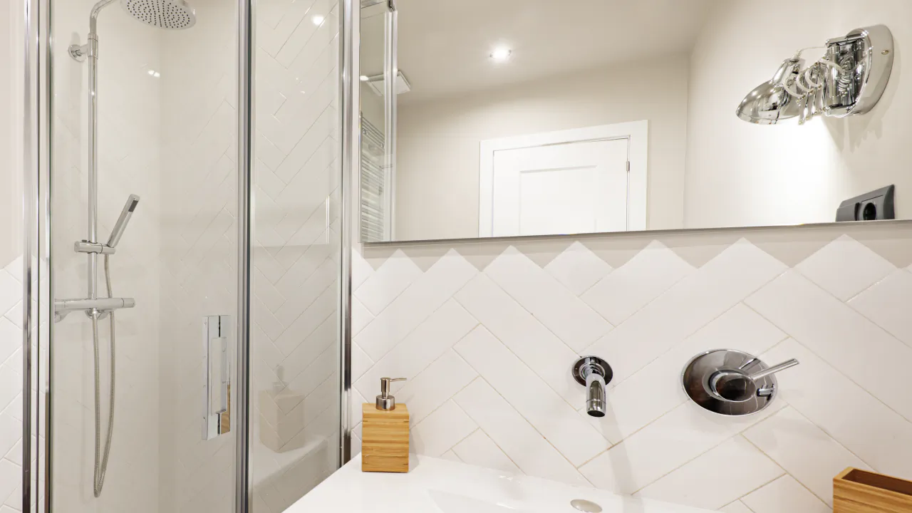 Finished bathroom with white herringbone tiles, a glass shower screen and chrome wall-mounted taps