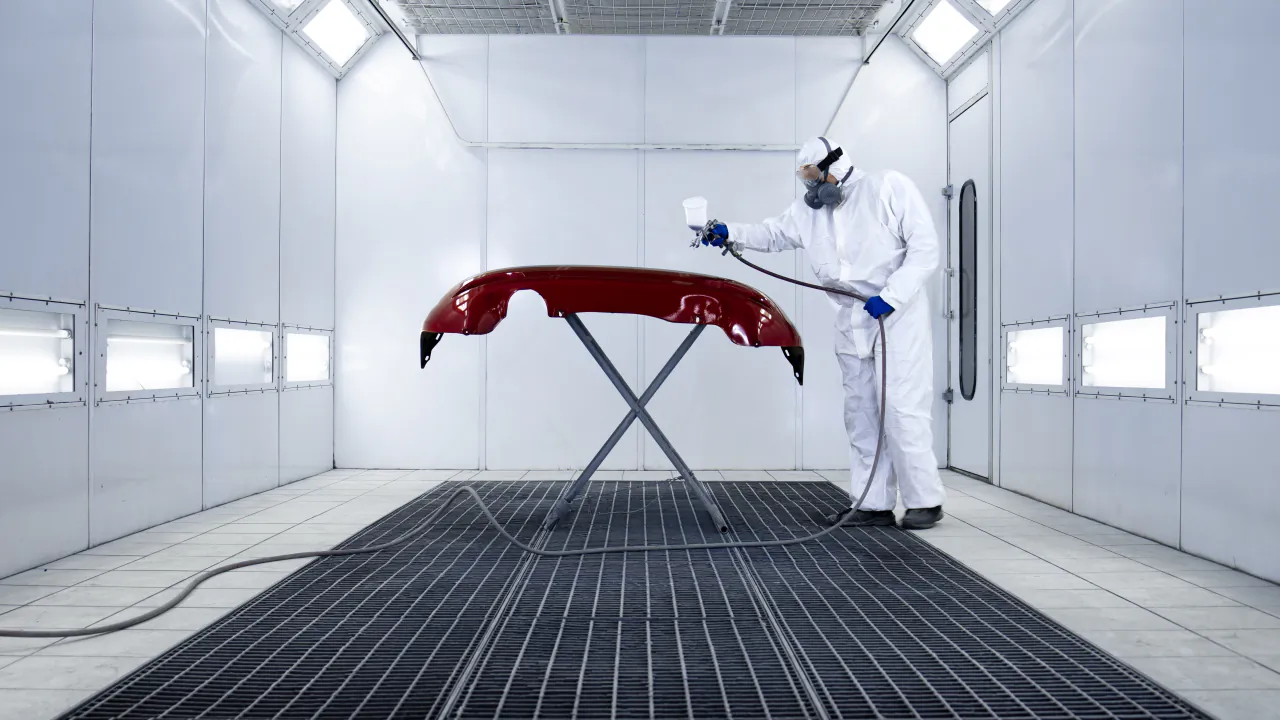 Body shop painter in a respirator spraying a red bumper on a stand inside a spray booth