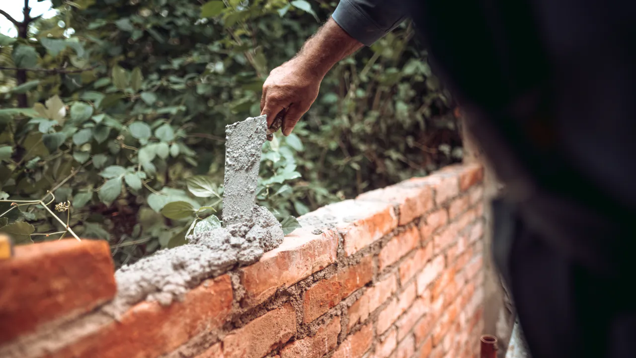 Bricklayer spreading mortar along a course of red bricks on a garden wall