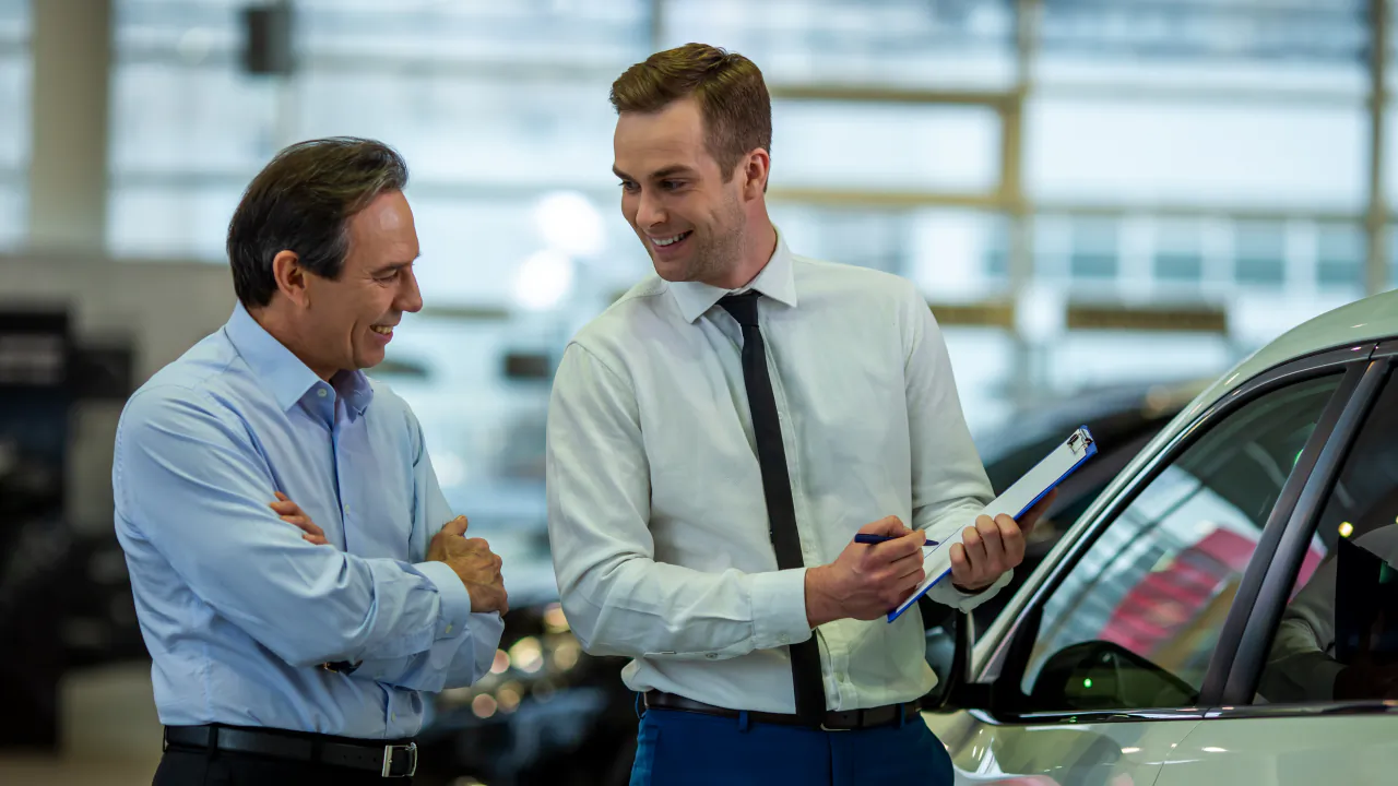 Salesperson with a clipboard talking a customer through a car in a bright showroom