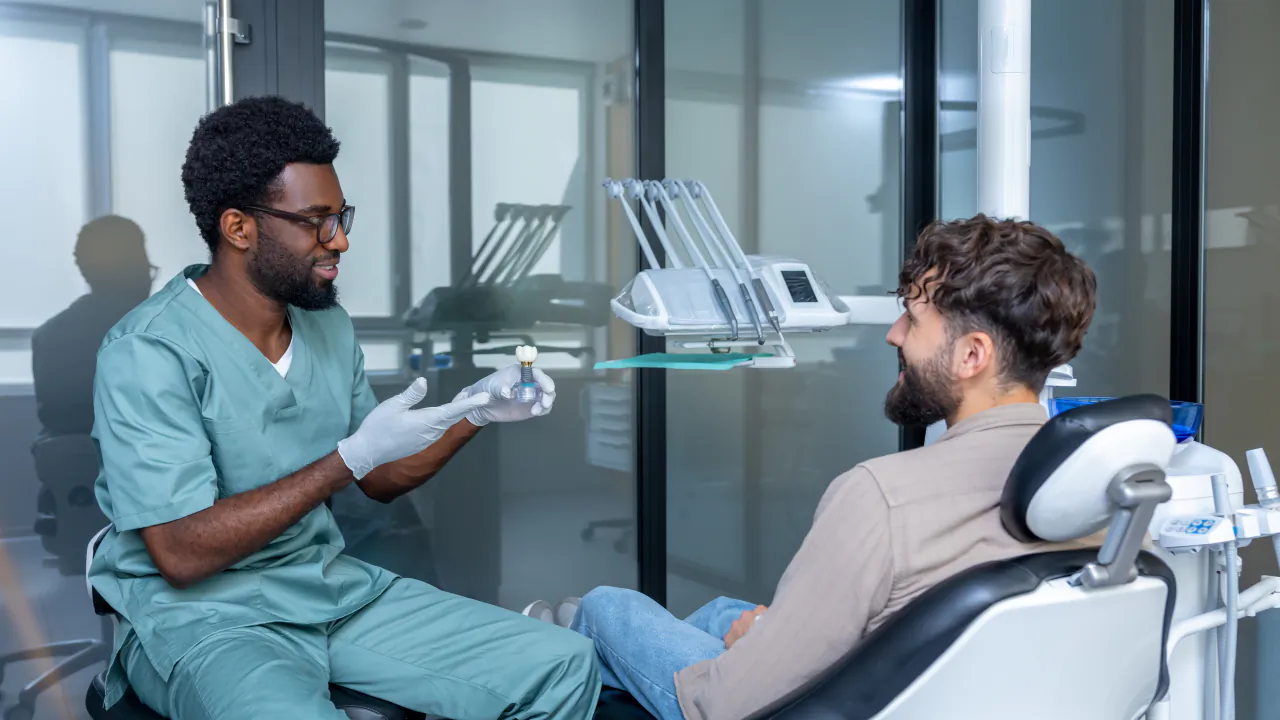 Dentist in green scrubs talking a patient through a check-up in a bright modern surgery