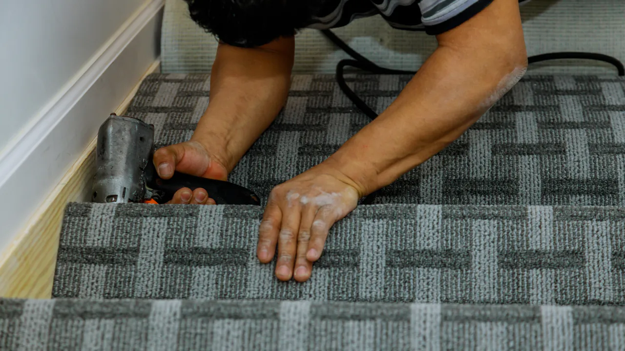 Carpet fitter fixing a grey patterned carpet onto a staircase with a staple gun