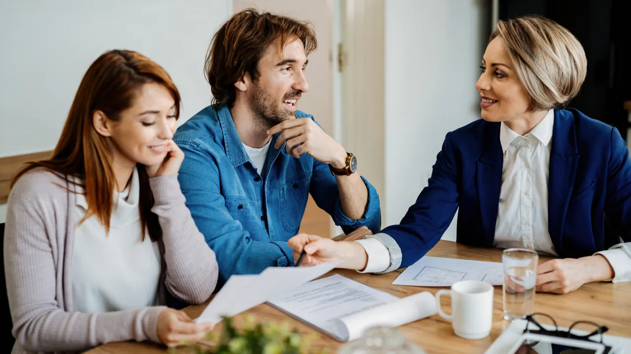 Insurance broker in a navy jacket talking a young couple through their policy documents