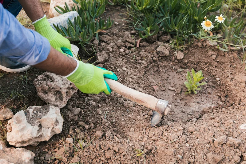 Close-up of a gloved hand digging a rockery bed with a hoe