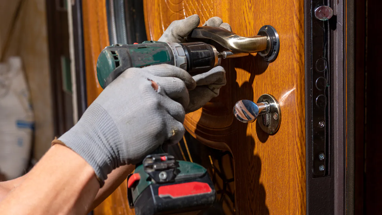 Locksmith in gloves fitting a new lock and handle to an oak-finish front door