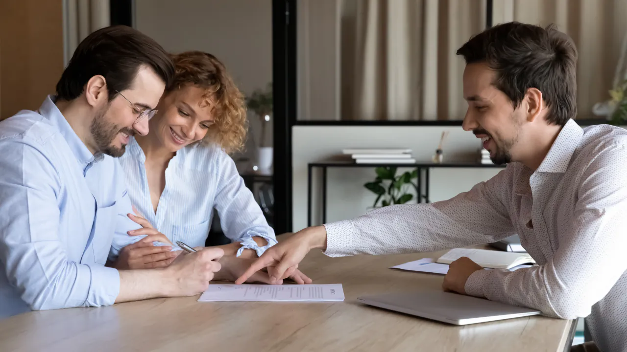 Mortgage adviser pointing out where a young couple should sign on their application