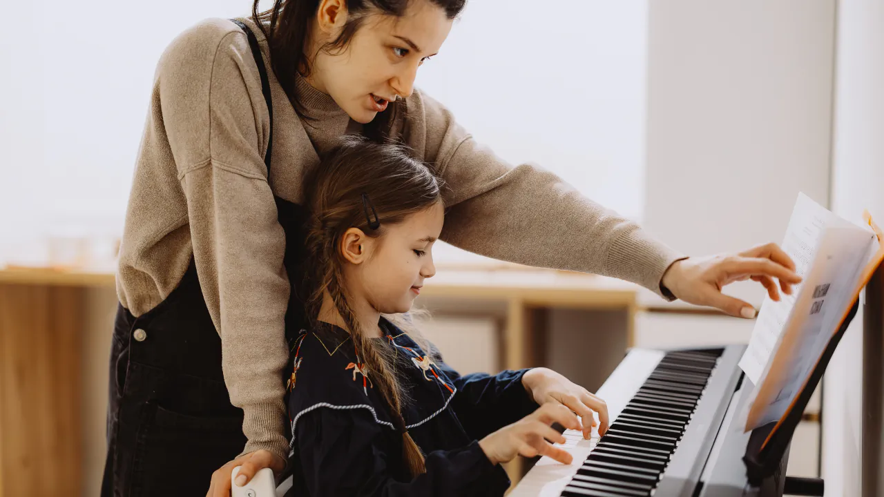 Piano teacher leaning in to guide a young pupil through a piece of sheet music