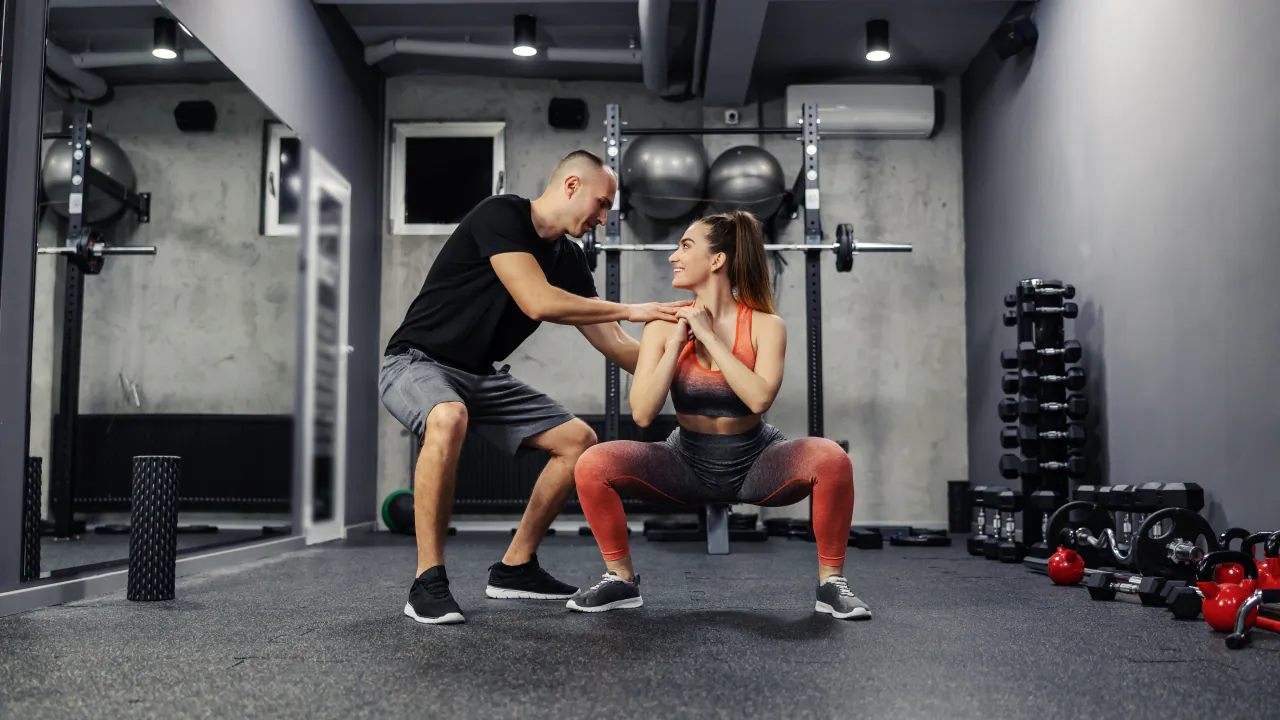 Personal trainer coaching a client through a squat in a small private gym