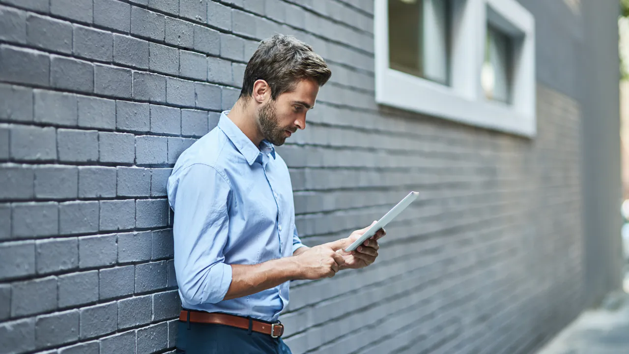 Property manager checking a tablet outside a grey brick apartment building