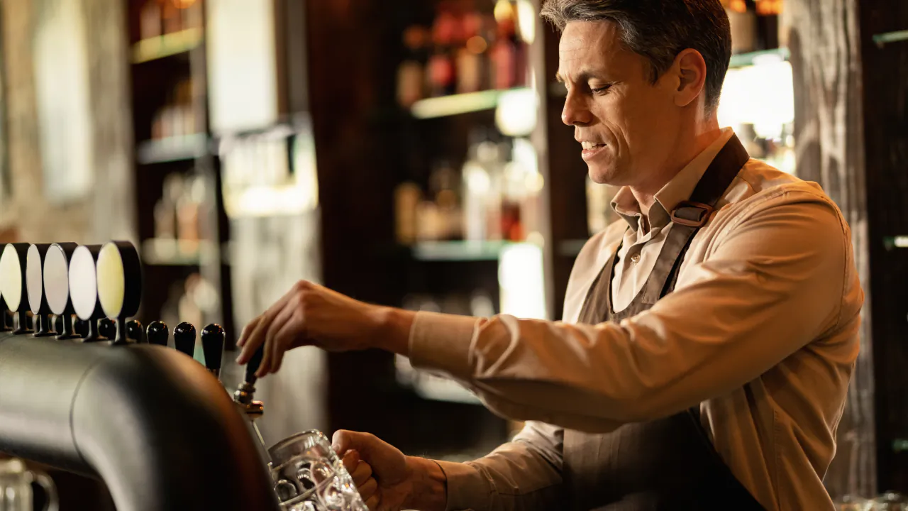 Bartender pulling a pint at the pumps of a warmly lit traditional pub