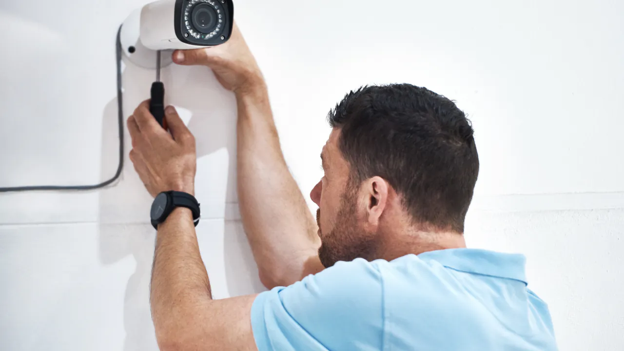 Security engineer fixing a white CCTV camera to the corner of a wall