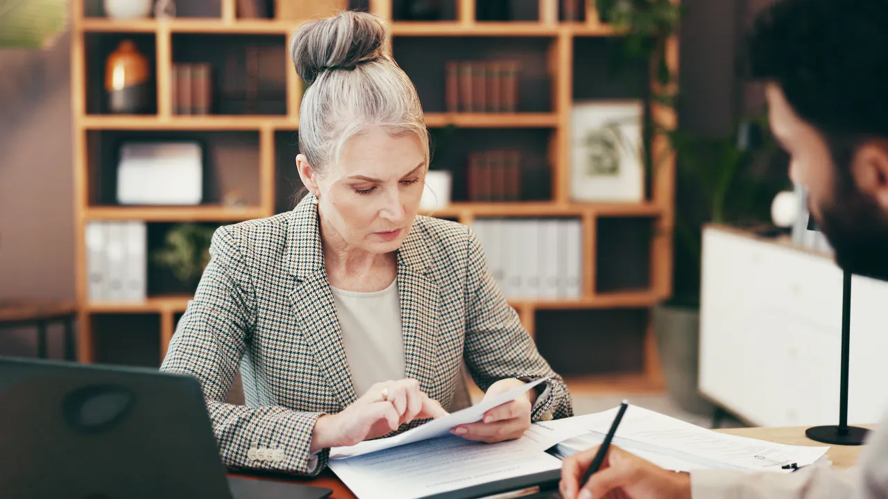 Solicitor reading through paperwork with a client across the desk in a book-lined office
