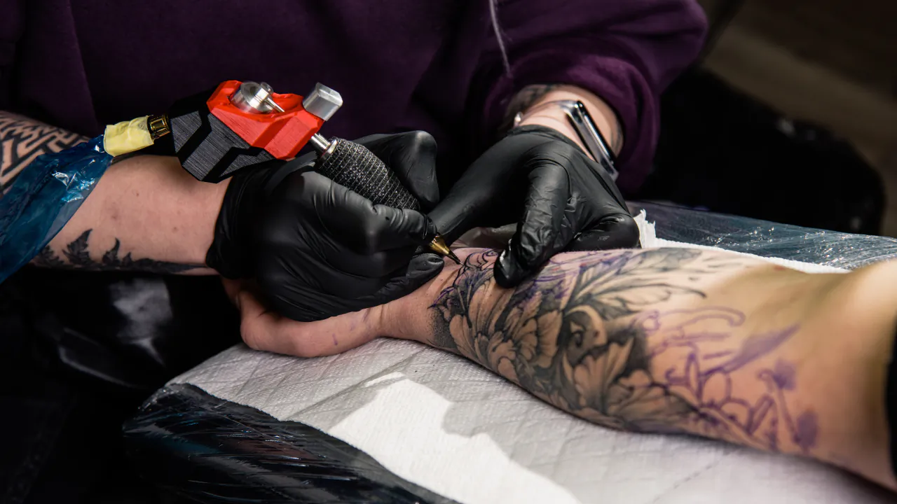 Tattoo artist in black gloves working a floral sleeve on a client's forearm