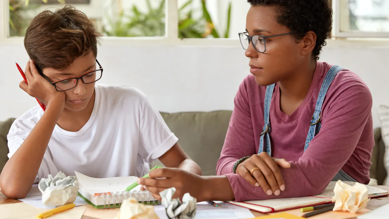 Tutor working through a problem with a teenage student at a table covered in notes
