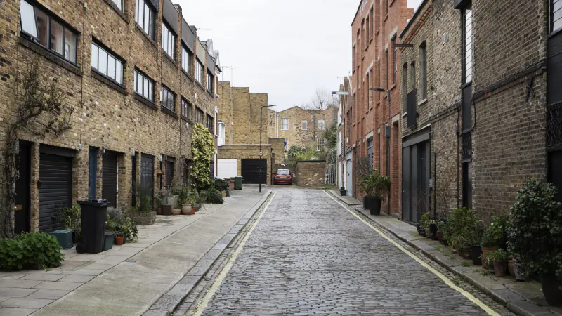A cobbled London mews lined with brick warehouses, planters and black garage doors