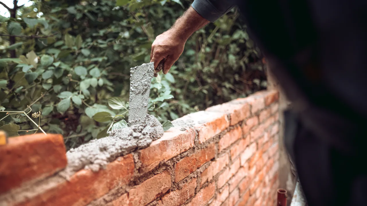 Bricklayer spreading mortar along a course of red bricks on a garden wall