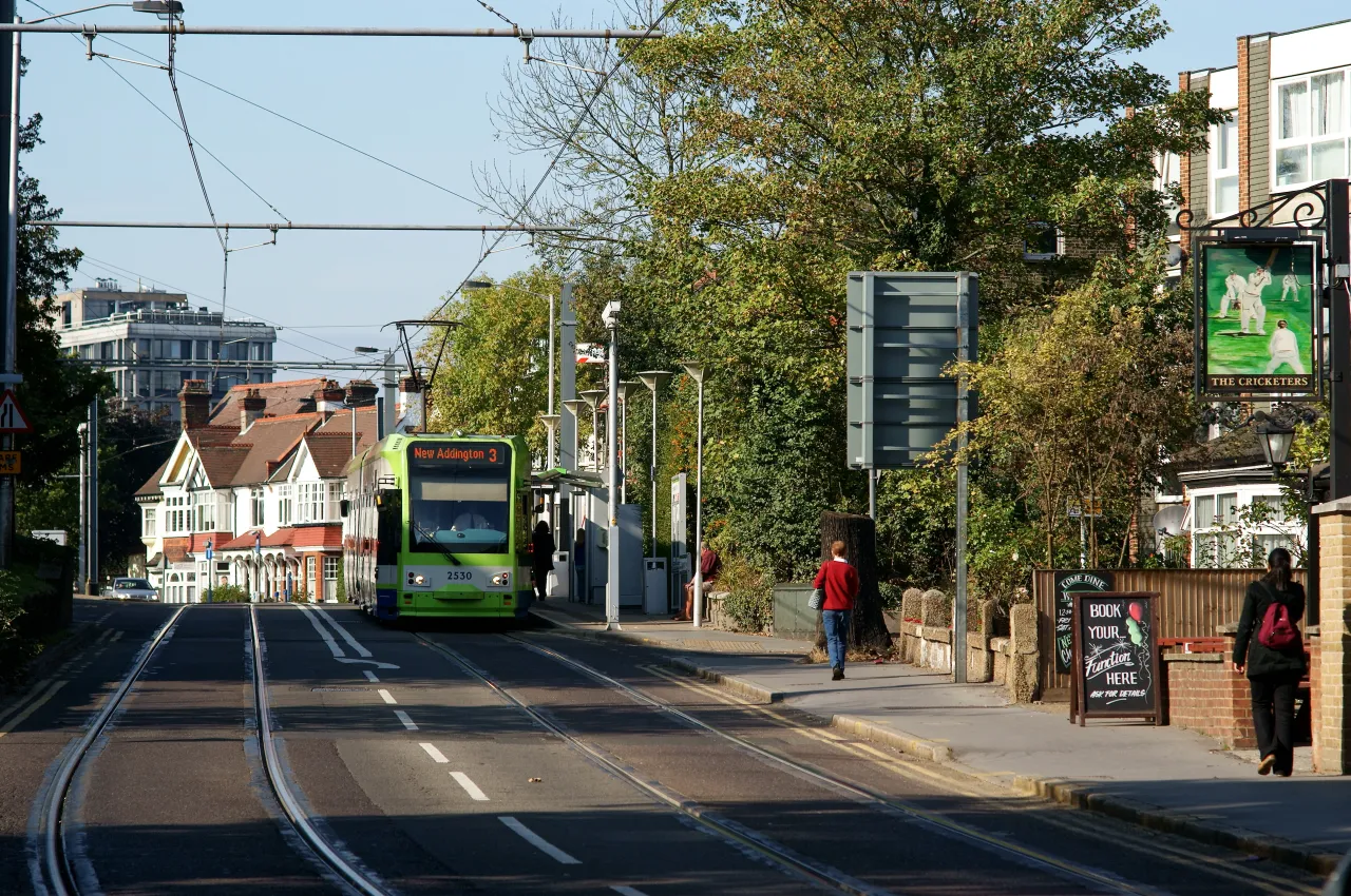 Tram running along Addiscombe Road past shops and pedestrians on a sunny day