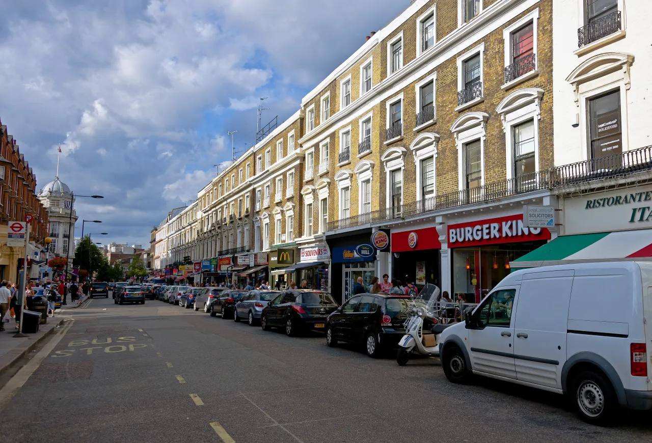 Queensway, Bayswater, looking north from the tube station with shops and pedestrians