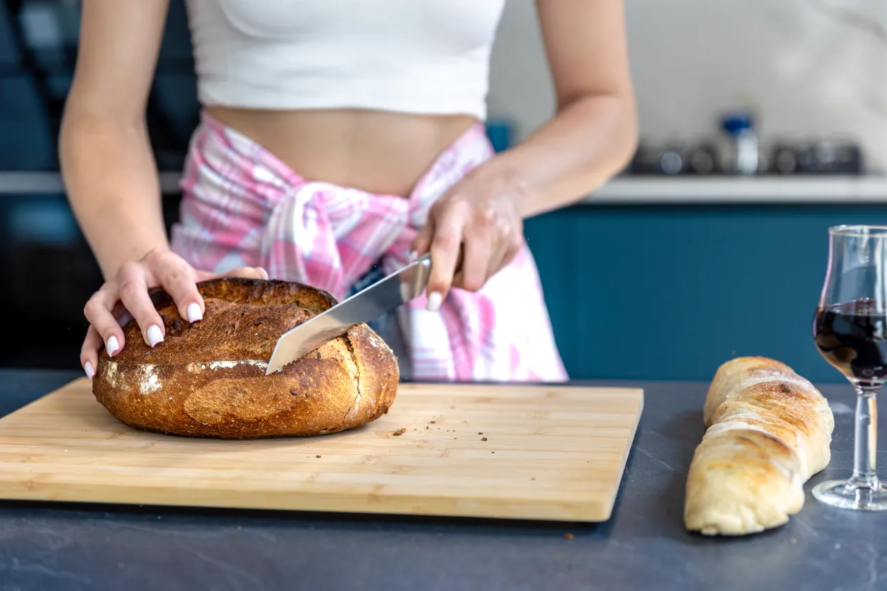 Host slicing a fresh loaf of home-baked bread on a wooden board in the kitchen, preparing breakfast