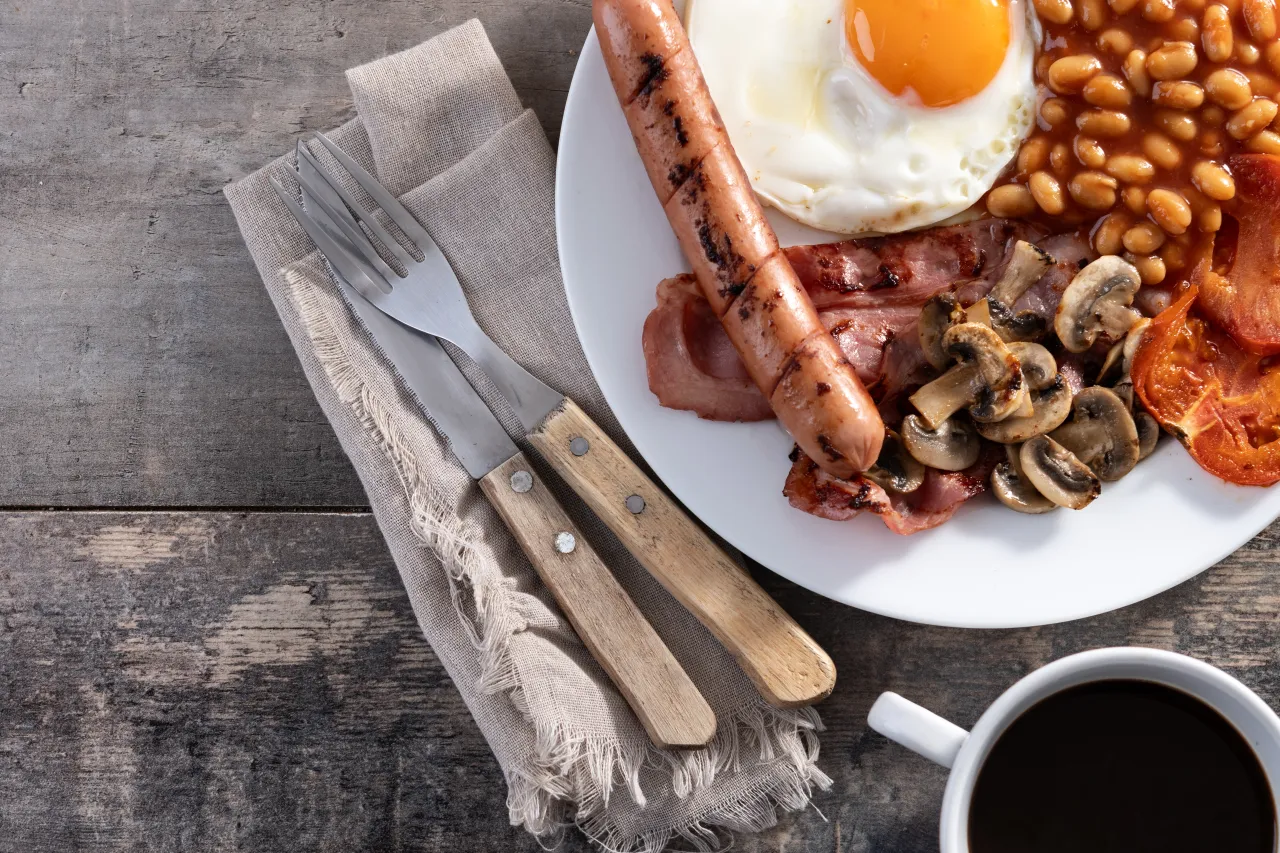 Full English breakfast plate with egg, bacon, sausage and mushrooms on a rustic wooden guest house table
