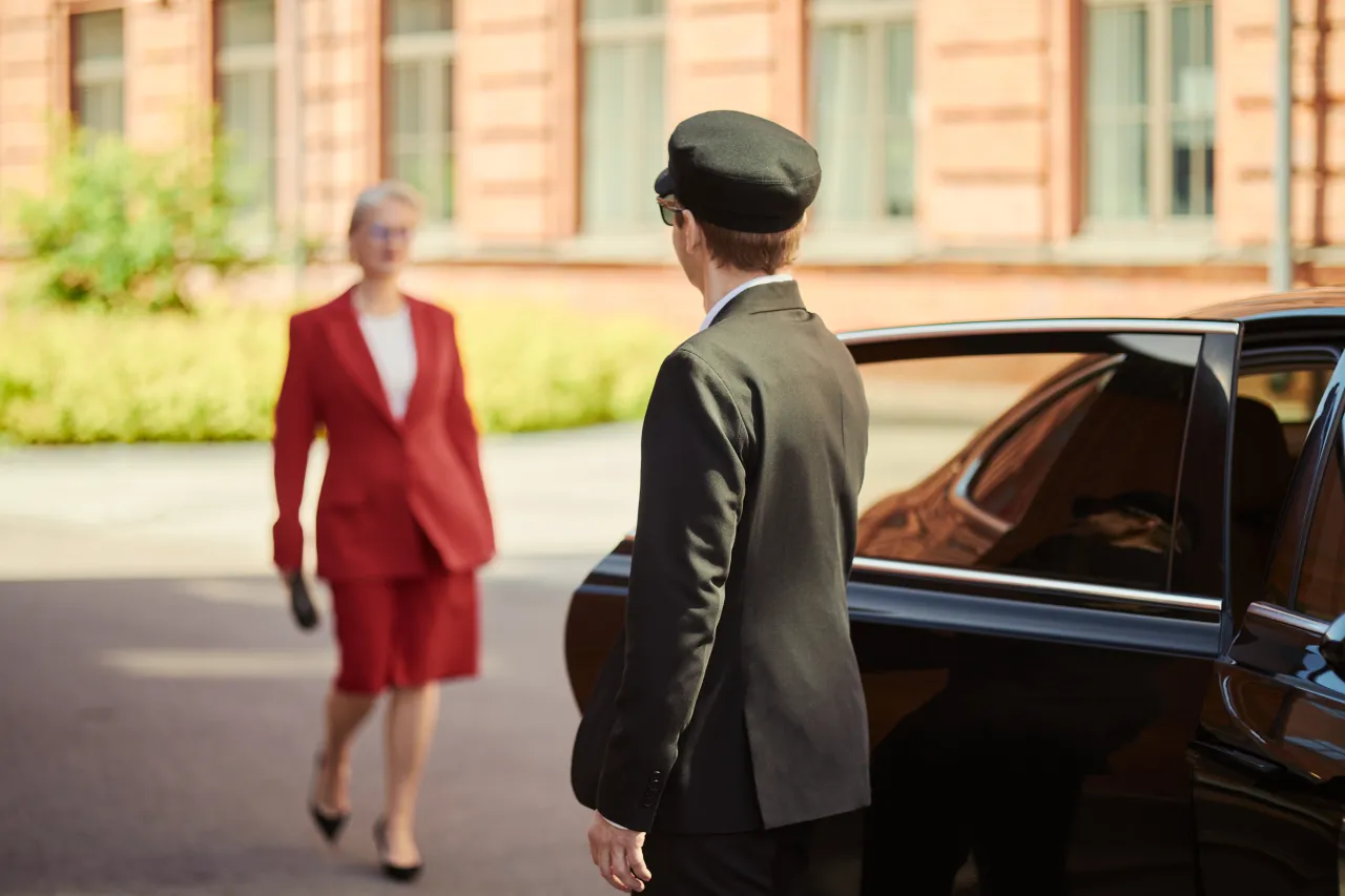 A uniformed chauffeur opening the car door for a client outside an elegant building