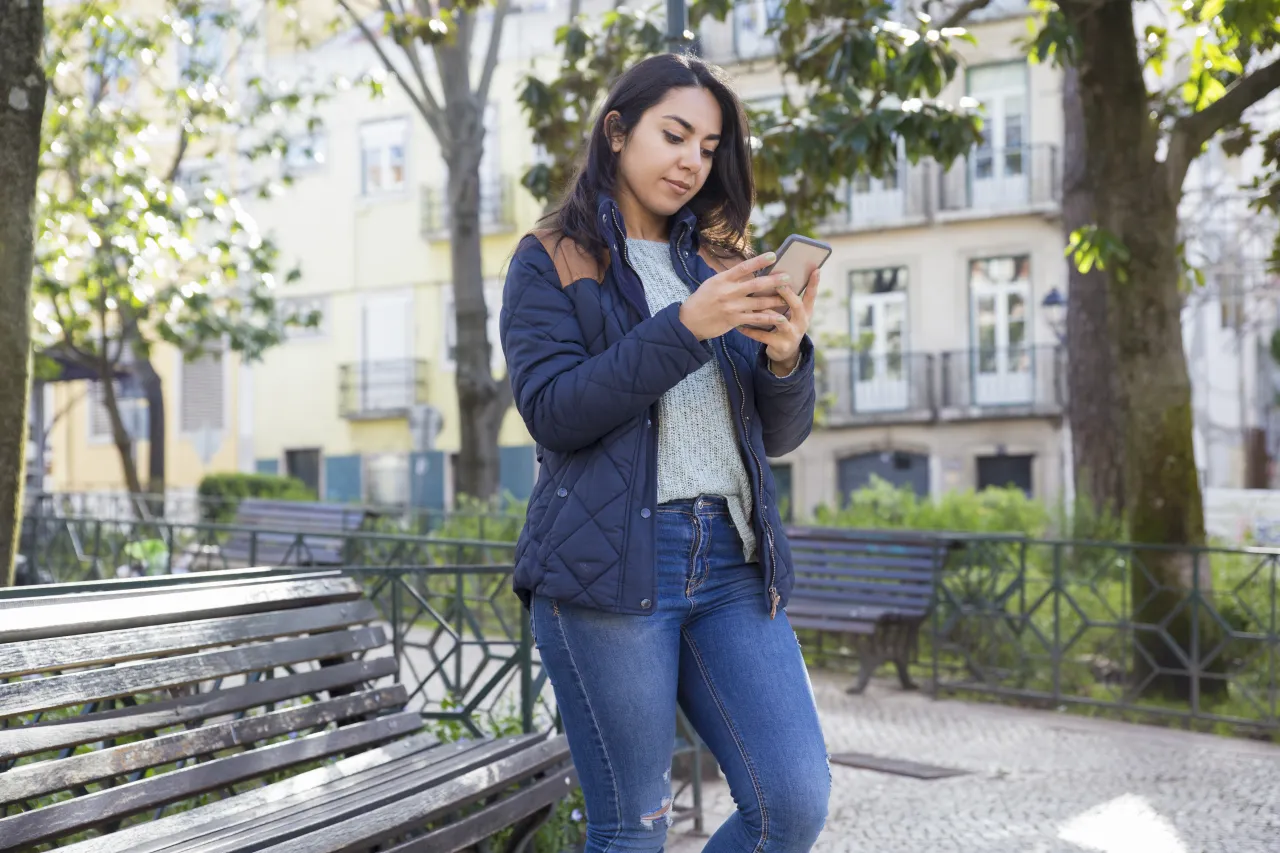 A woman checking her phone on a European street, searching for a minibus or coach hire company