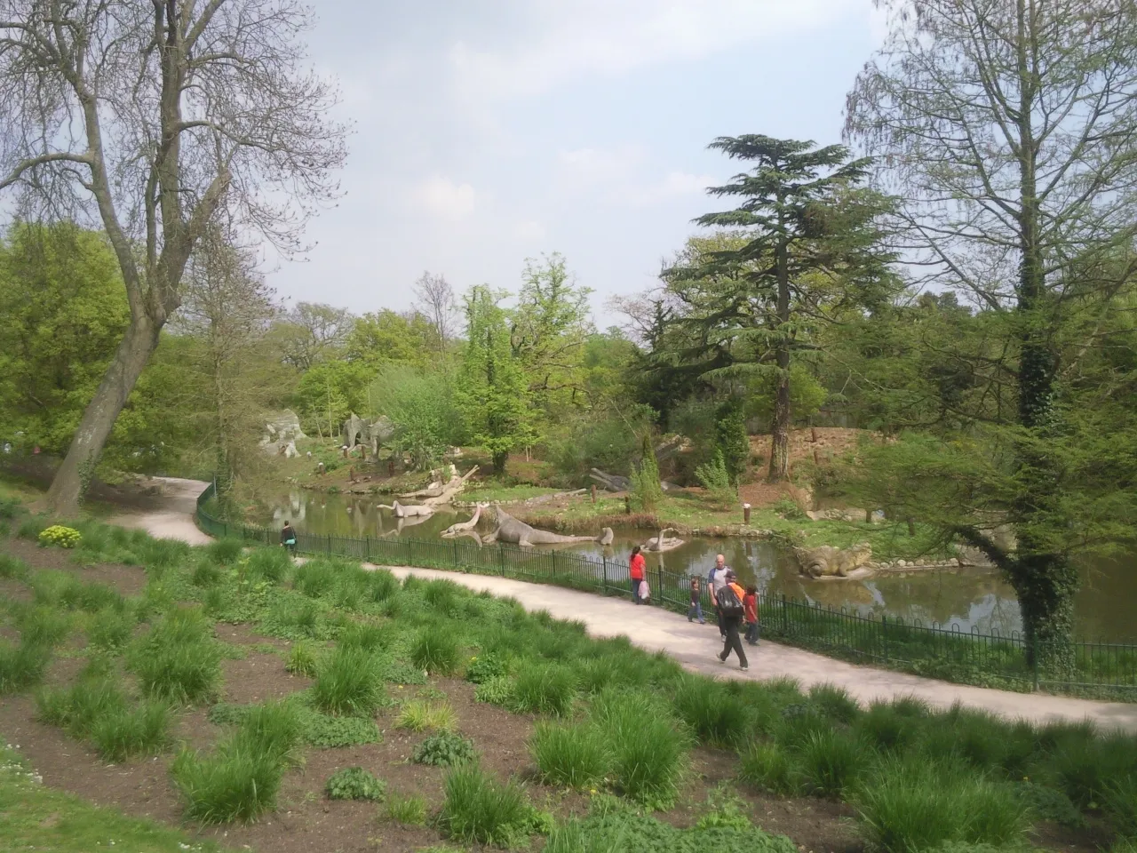 Visitors walking beside the dinosaur lake in Crystal Palace Park