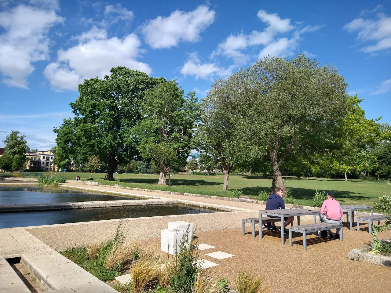 The New River pond and bridge in Town Park, Enfield, with people relaxing nearby