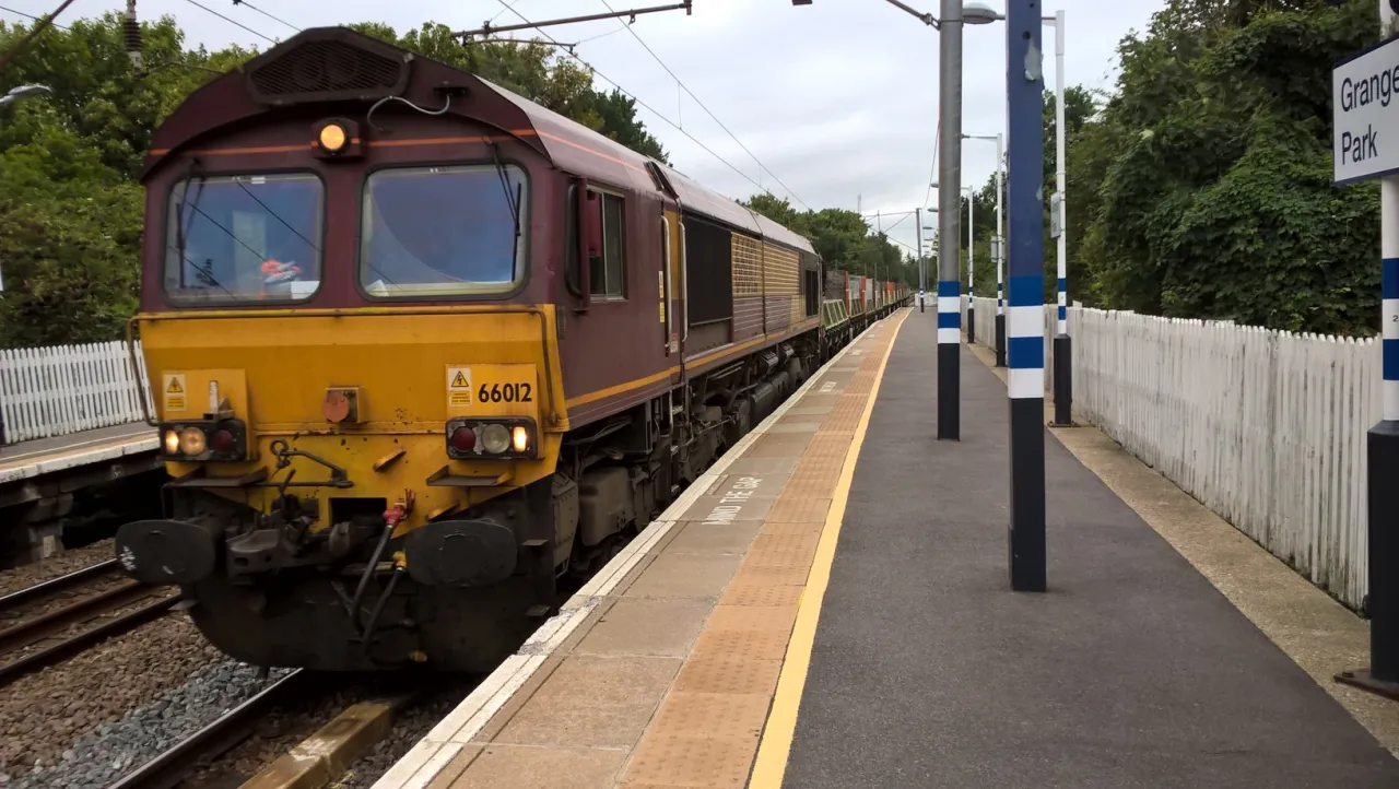 A freight train passing through Grange Park's single station, Enfield
