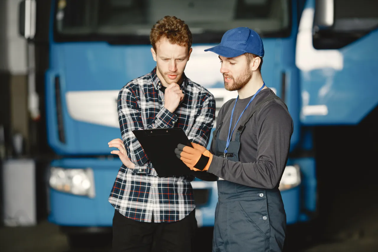 Haulage yard worker and driver reviewing a clipboard of booking details beside a lorry