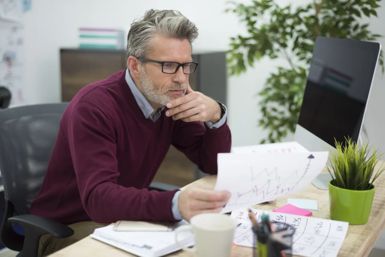Planning consultant reviewing a report and a chart at his desk, thinking through a case