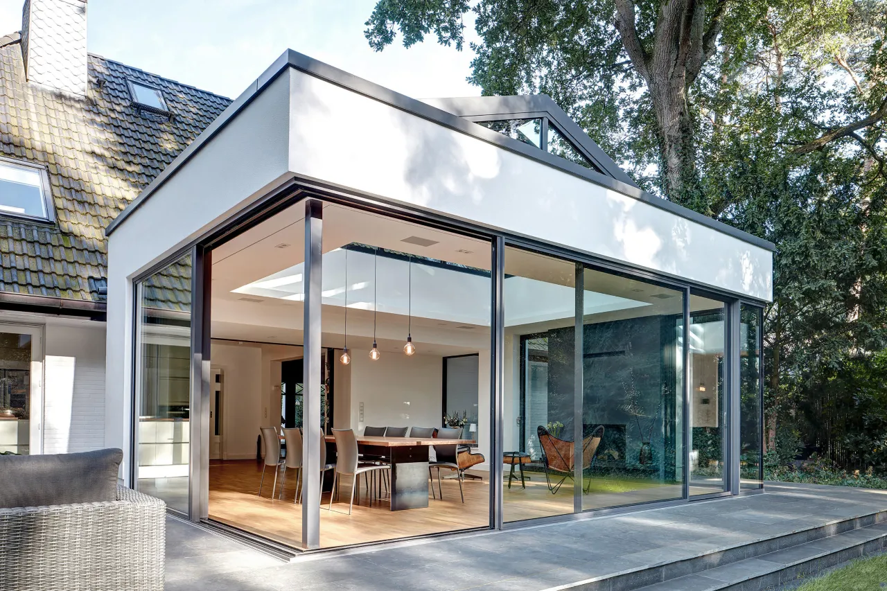 A completed glass and steel-framed house extension opening onto a garden