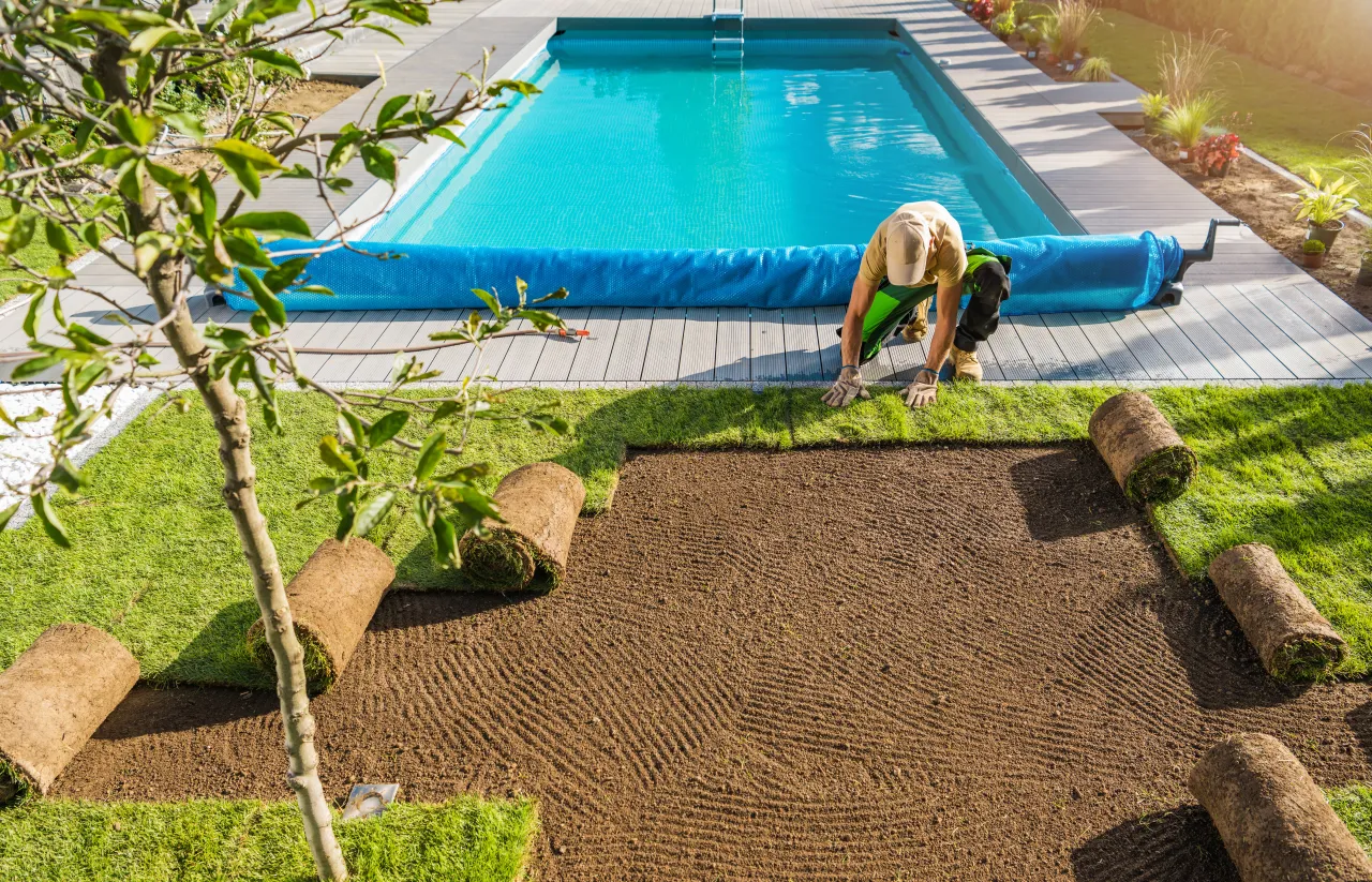 A finished garden pool with a worker laying new turf around the edge, the last finishing touches after the build itself is done