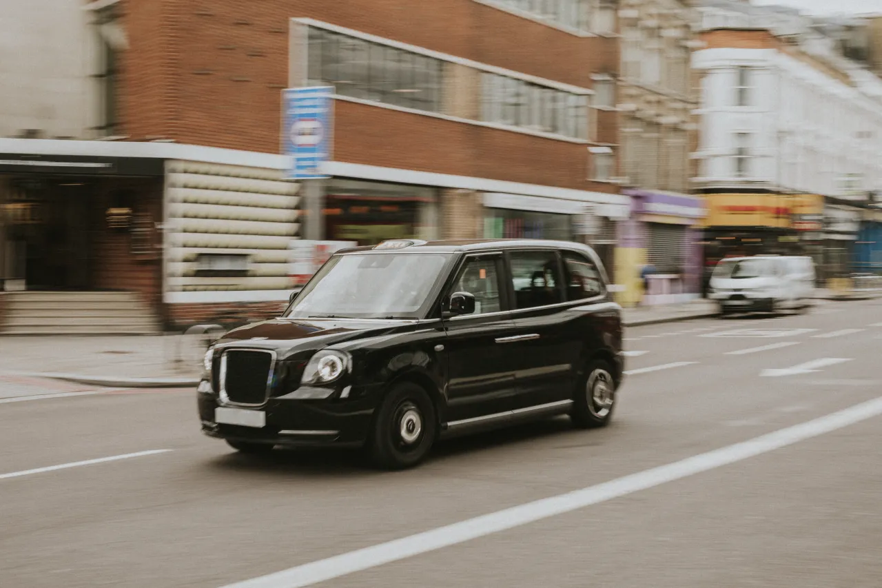 A traditional black cab taxi driving along a London street, in motion, working