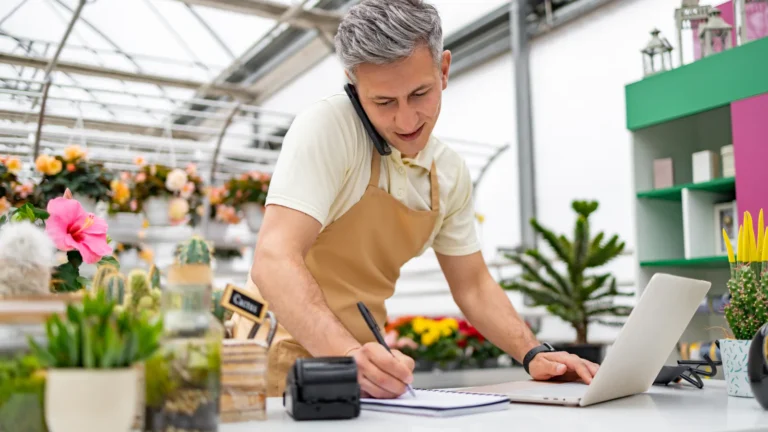 A garden centre owner taking an order on the phone while working at a laptop