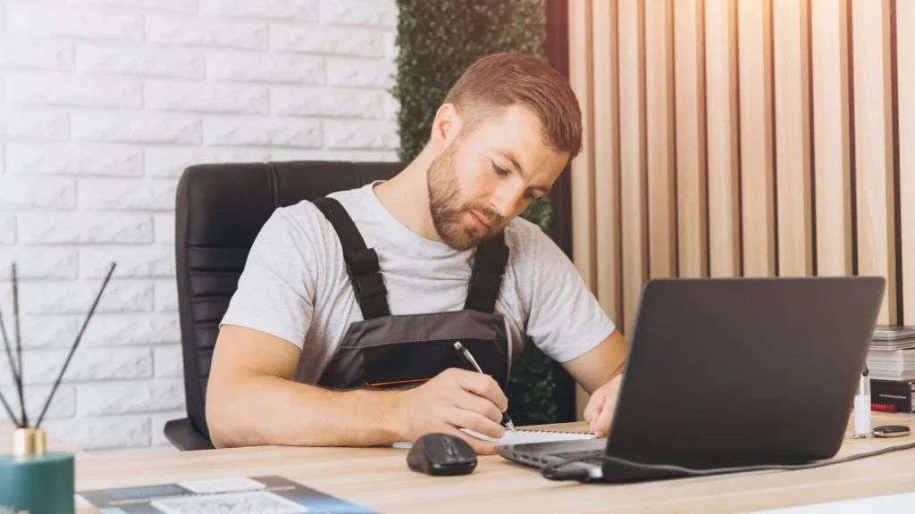A garage manager making notes in front of a laptop in the workshop office