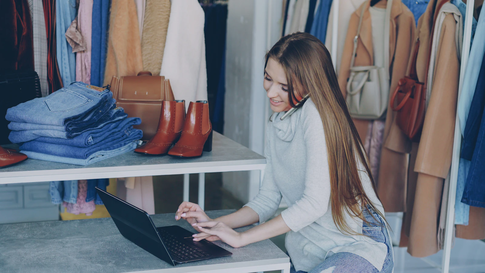 A shop owner working on a laptop at a counter surrounded by rails of clothes