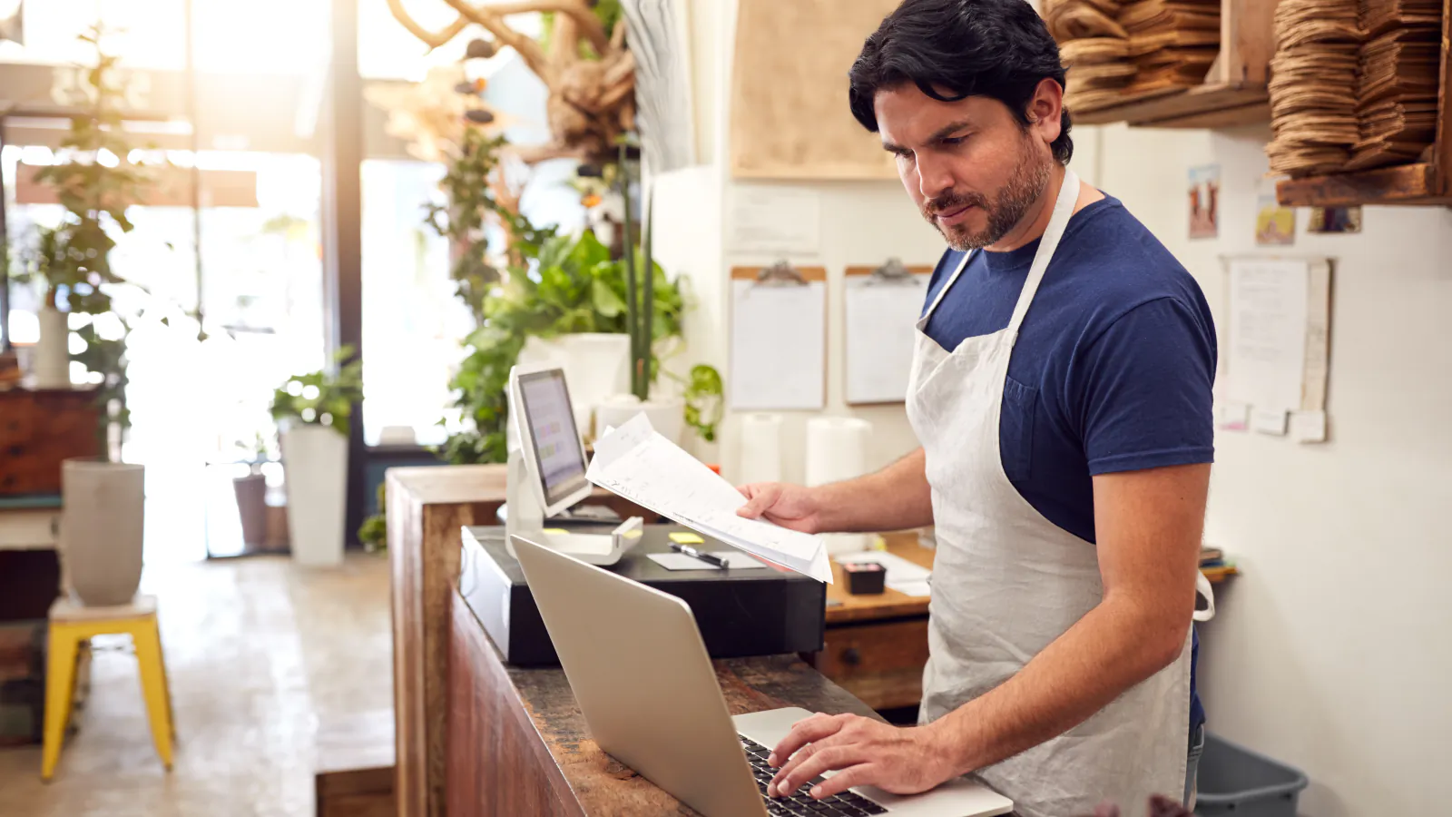 A florist working on a laptop behind the counter of his shop